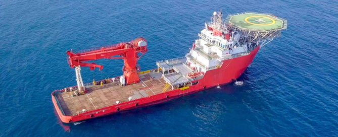 Aerial image of a medium-size red offshore supply ship with a helipad and a large crane